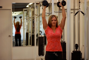 Stephanie Aikin lifting free weights over her head.